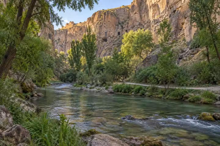 River and walking path beneath the sunlit cliffs of Ihlara Valley in Cappadocia