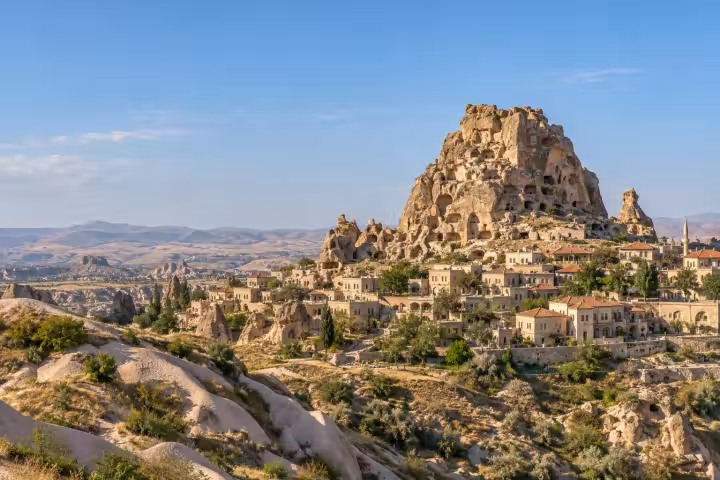 Uchisar rock citadel above stone houses and pale Cappadocia ridges in daylight