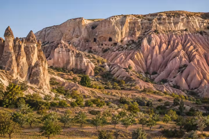 Cappadocia cave openings and pink valley cliffs above green orchards