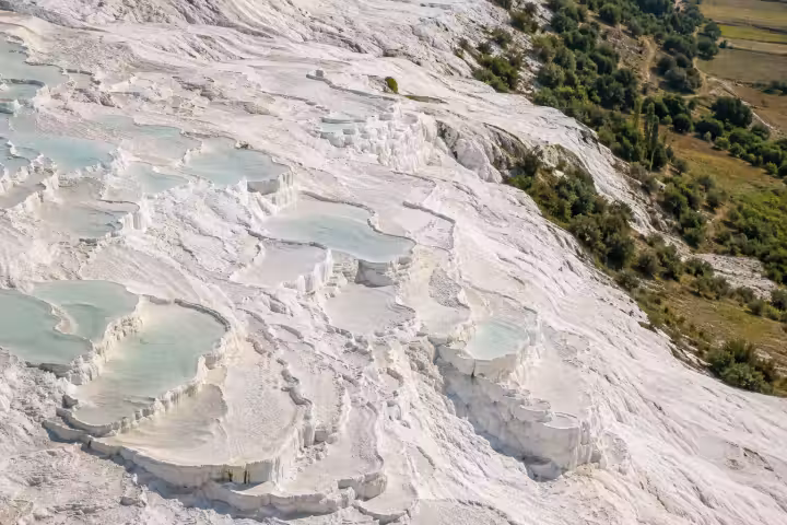Elevated view of white Pamukkale terraces and pale blue pools beside green countryside