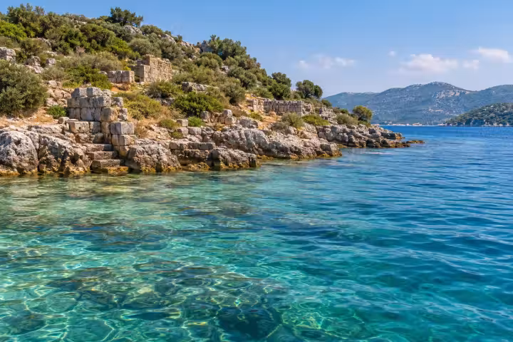 Stone walls and steps along Kekova shoreline beside clear turquoise water
