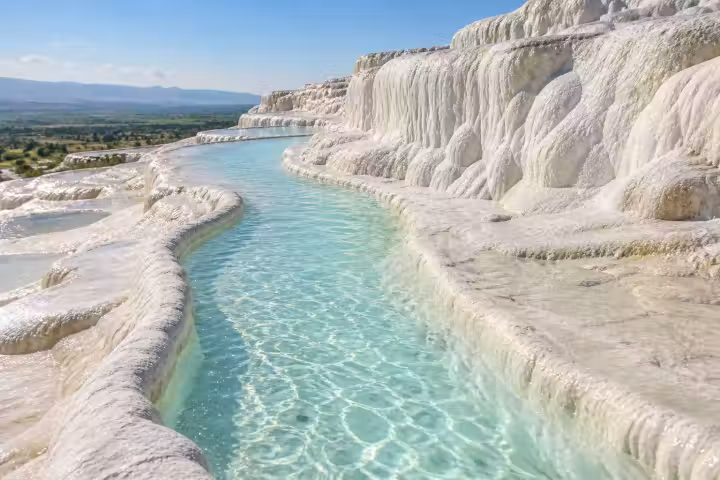 Curving turquoise water between white Pamukkale travertine terraces above the green plain